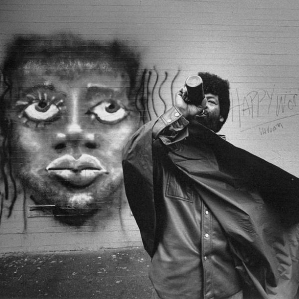 A man drinks wine while standing in front of graffiti face painted on a wall. For a San Francisco Chronicle article, "New Bohemia," about a trendy section of San Francisco's Mission District.