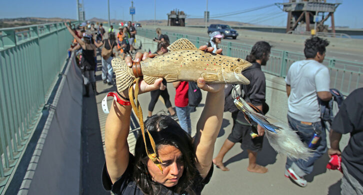 Carquinez Strait, CA — Desirae Harp (Mishewal OnastaTis Nation) holds up a wooden salmon figurine as the Run4Salmon crosses over the Benicia-Martinez Bridge. September 17, 2018. Tom Levy/The Spiritual Edge